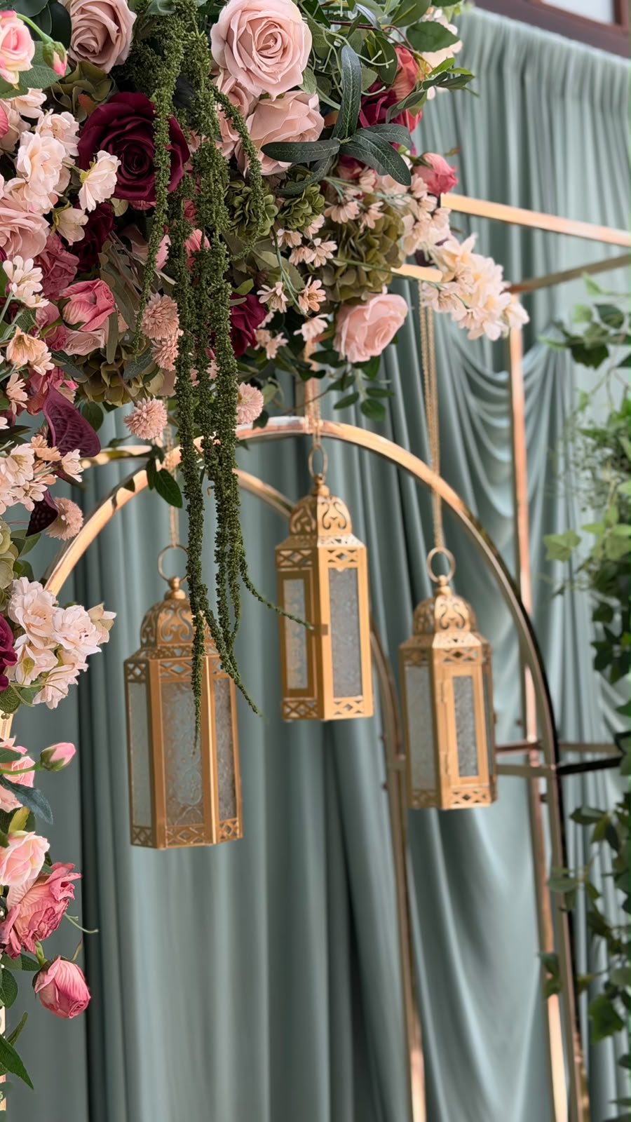 Three brass lanterns hanging inside an arch, under a cascade of roses
