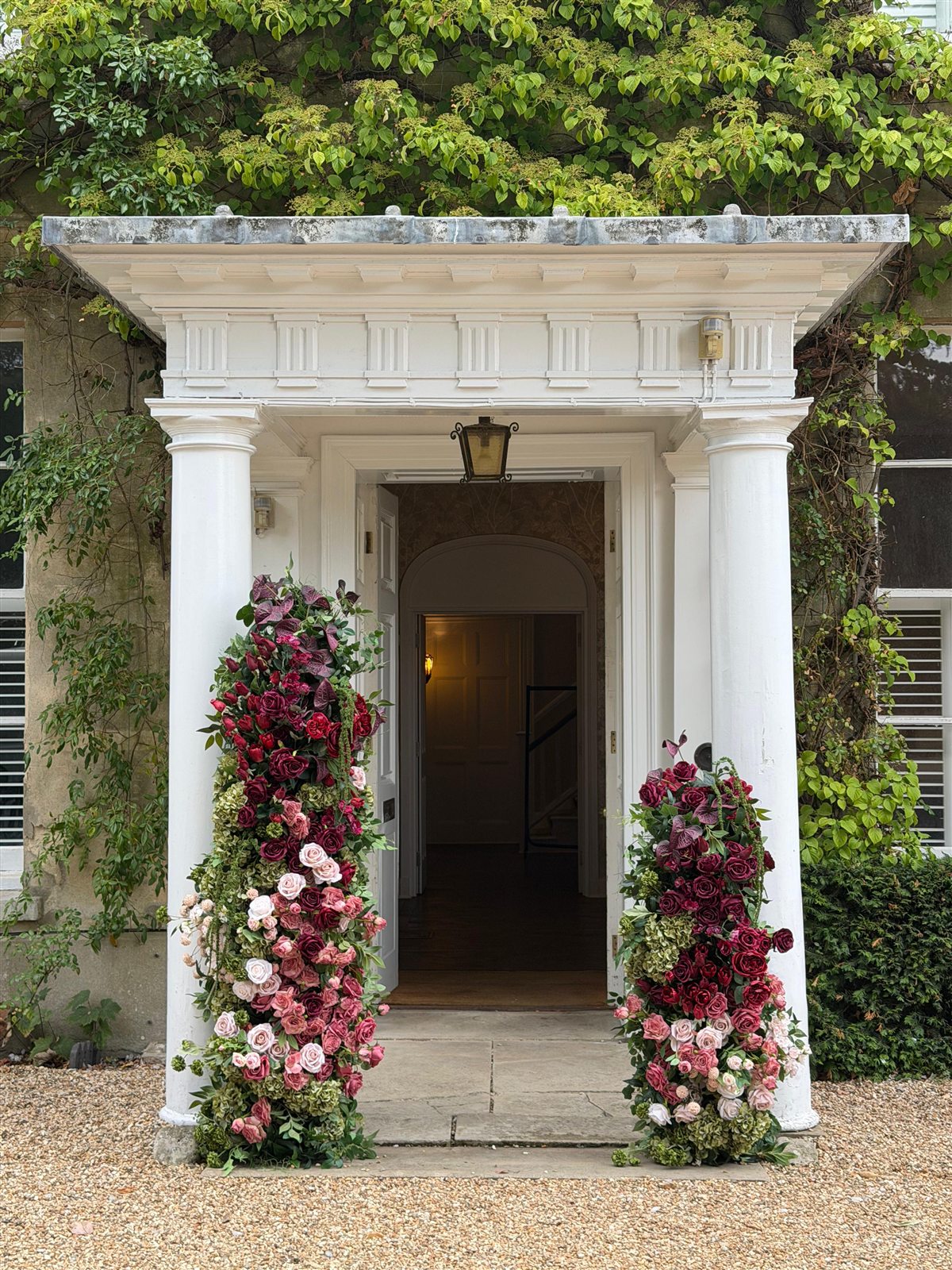 A white columned manor porch framed by two tall columns of burgundy and blush roses